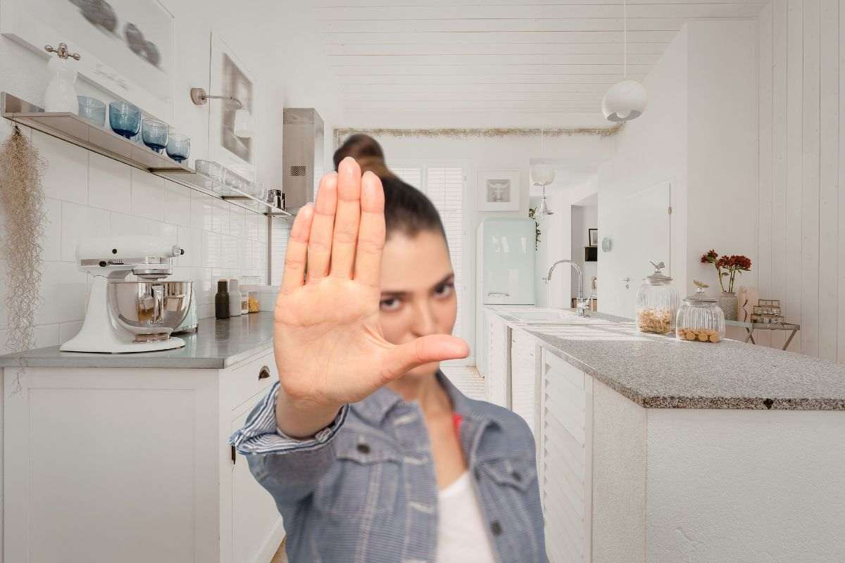 donna in primo piano che dice stop ad una cucina completamente bianca
