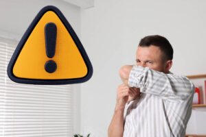 uomo che copre il naso con un braccio e segnale di attenzione giallo