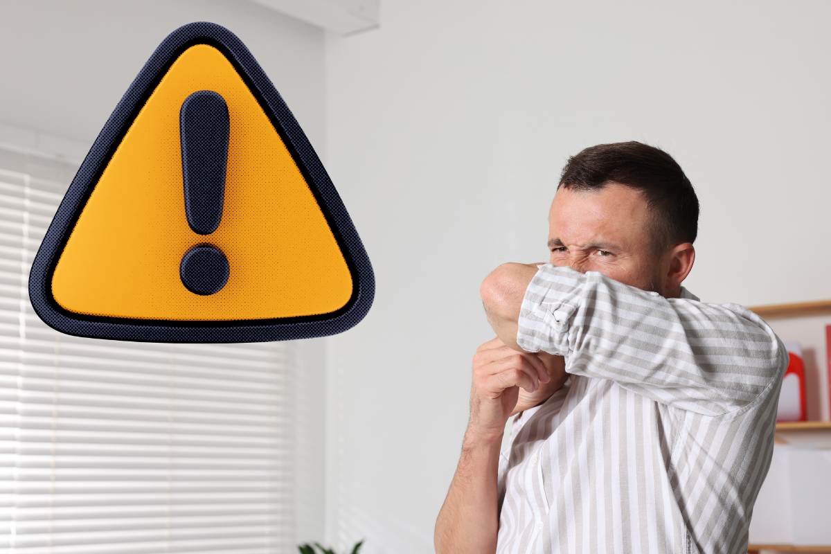 uomo che copre il naso con un braccio e segnale di attenzione giallo