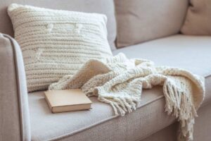 plaid in lana, cuscino bianco e libro, posizionati su un divano