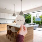 ampia cucina moderna con isola e mano che mantiene un bigliettino con scritta oops