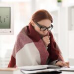 donna con coperta sulle spalle e termostato che indica 20 gradi