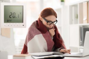 donna con coperta sulle spalle e termostato che indica 20 gradi