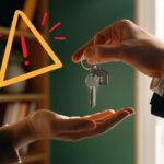 Una persona che passa delle chiavi di casa ad una persona ed un segnale di pericolo in alto a sinistra