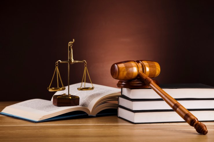 Un tavolo con sopra un libro di legge, una bilancia di giustizia ed un martello da giudice