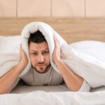uomo con coperte in testa perché non riesce a dormire