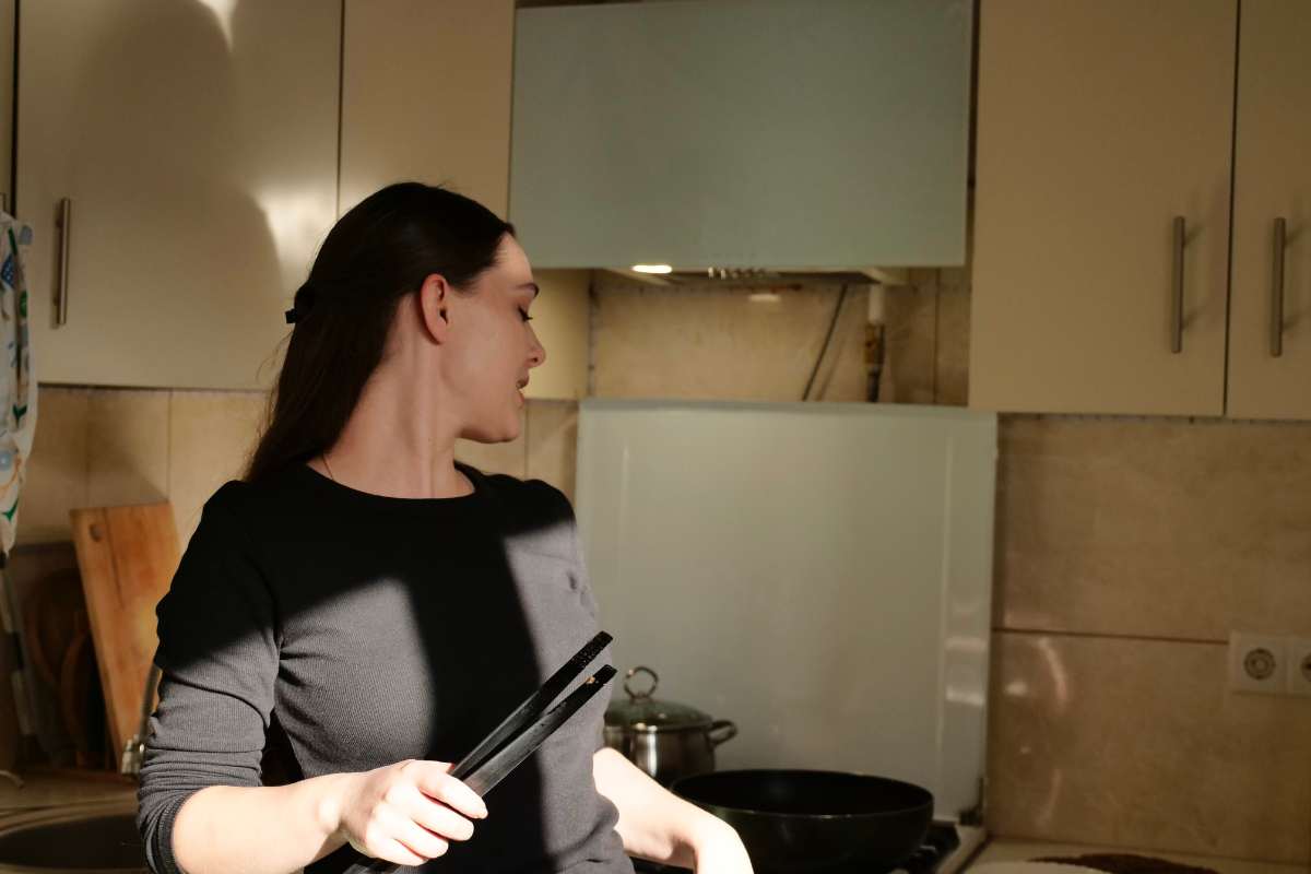 donna in cucina con delle pinze mentre cucina