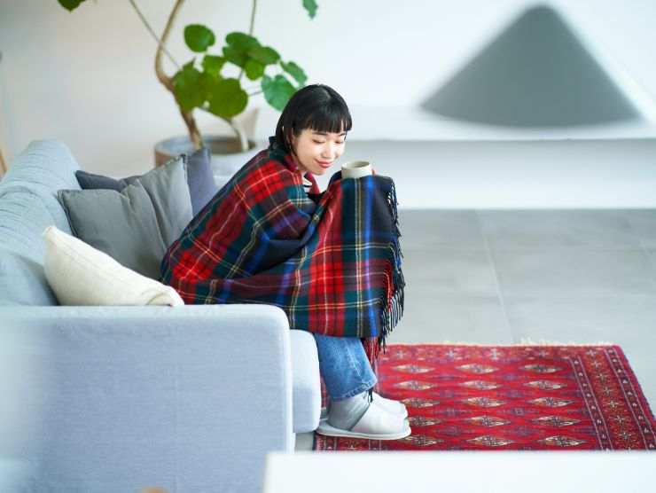 donna seduta su in divano avvolta in una coperta rossa a quadri