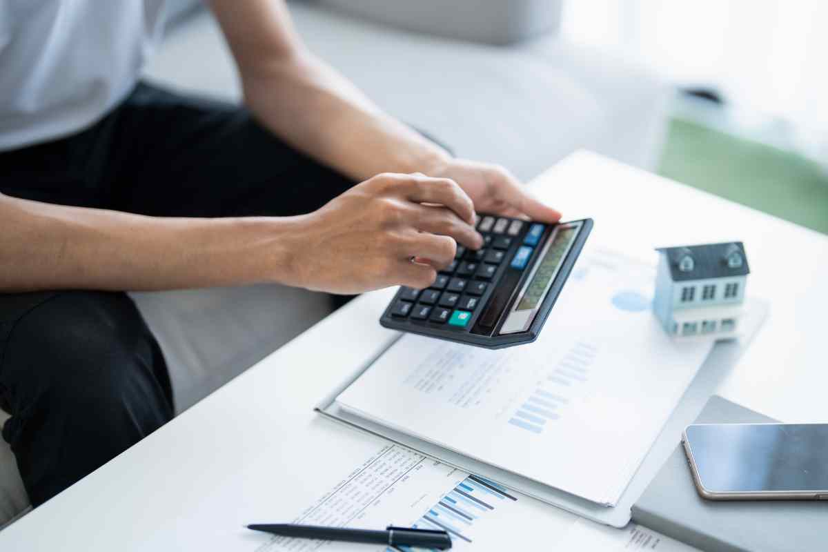 mano che fa conti sulla calcolatrice e vari fogli