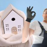 idraulico che fa segno ok con la mano e sullo sfondo casa con sciarpa