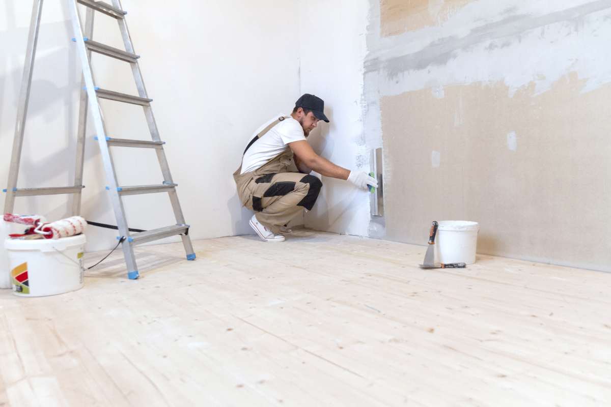 muratore che dipinge muro con scala alla sue spalle