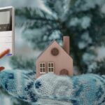 casa coperta con una sciarpa per il freddo e mano che tocca un termostato