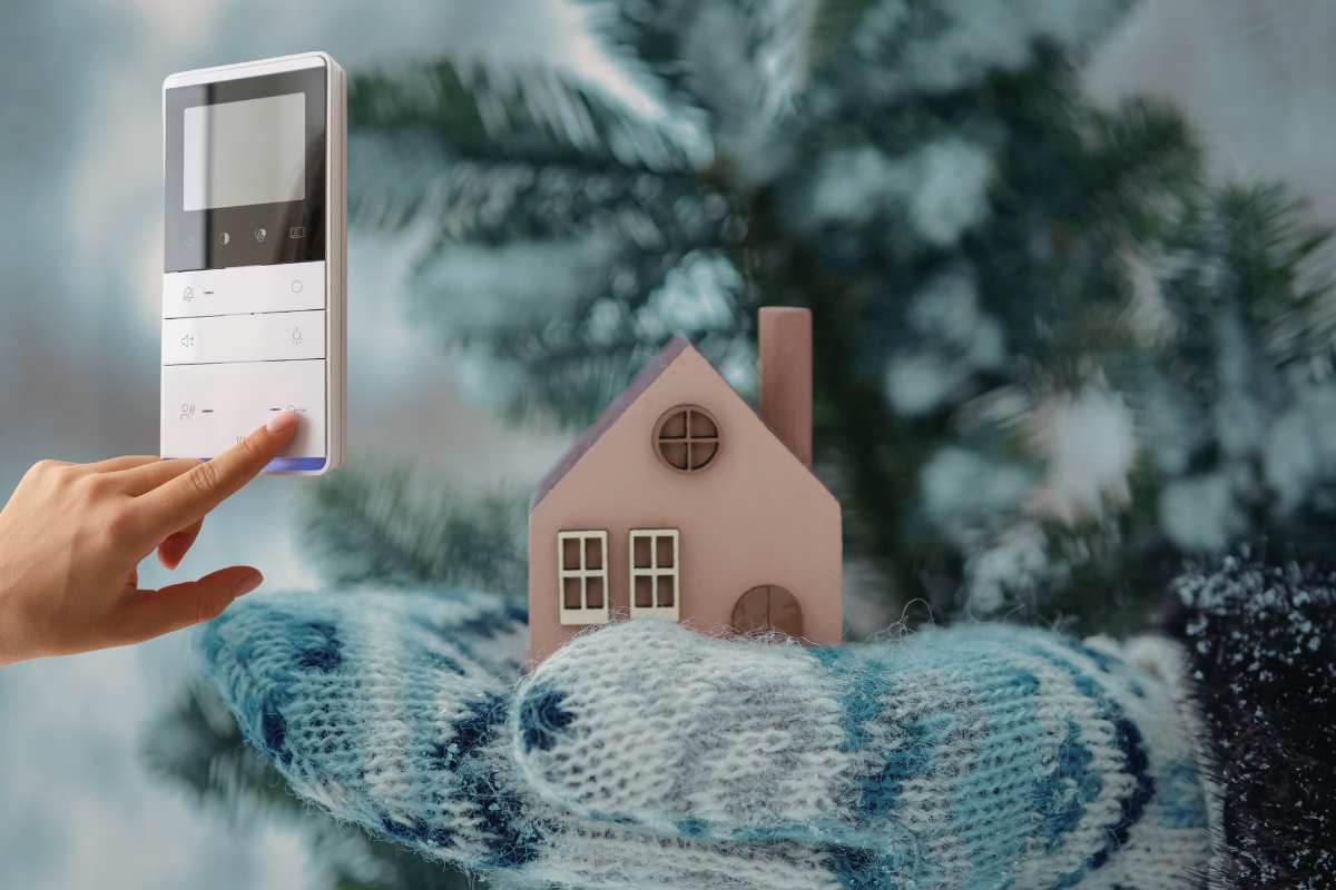 casa coperta con una sciarpa per il freddo e mano che tocca un termostato