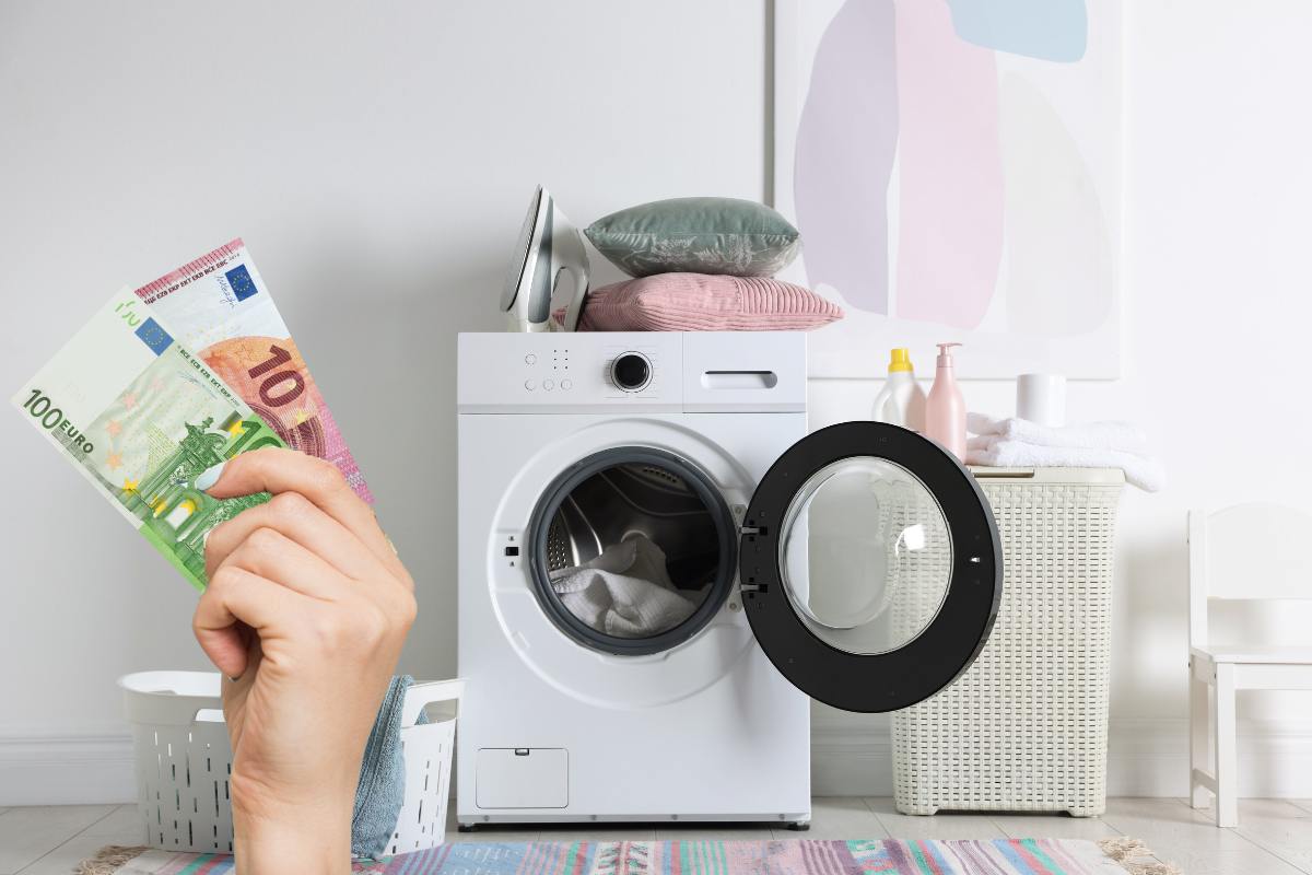 Una lavatrice aperta con una mano sulla sinistra che tiene una banconota da 100 ed una da 10 euro