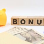 Una scrivania con sopra un salvadanaio, una scritta "bonus" dei soldi ed una calcolatrice