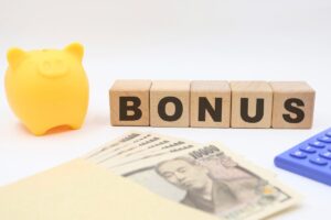 Una scrivania con sopra un salvadanaio, una scritta "bonus" dei soldi ed una calcolatrice