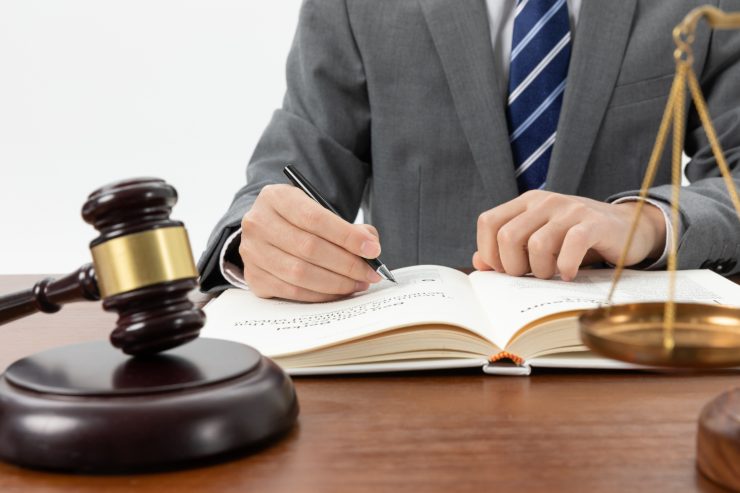 Una persona che scrive su un libro con davanti un martello da giudice