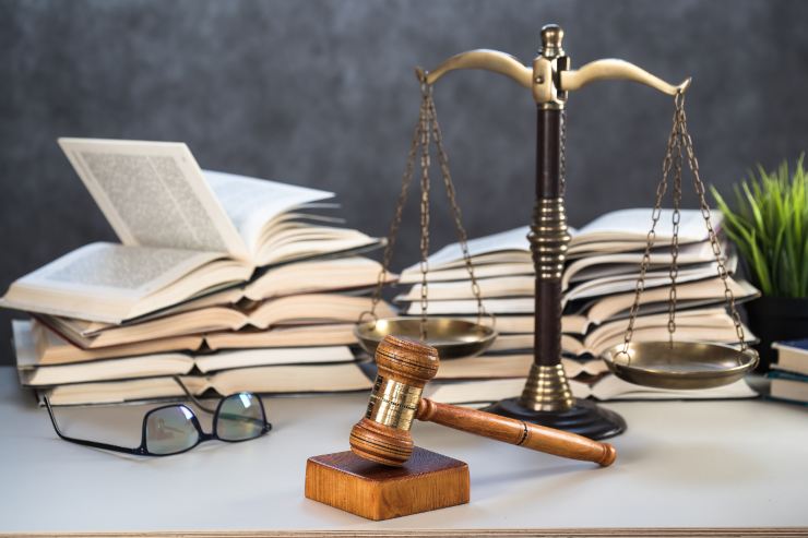 Un tavolo con sopra libri di legge, bilancia di giustizia e un martello da giudice