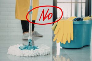 Una persona che pulisce i pavimenti con il mocio ed una scritta "No" in primo piano