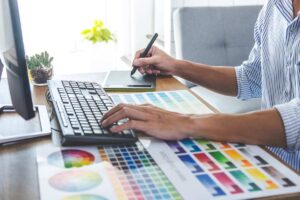 Un designer al computer che lavora con fogli con sopra diverse tonalità di colore.