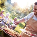 Un uomo che fa il barbecue per la famiglia seduta al tavolo in un giardino