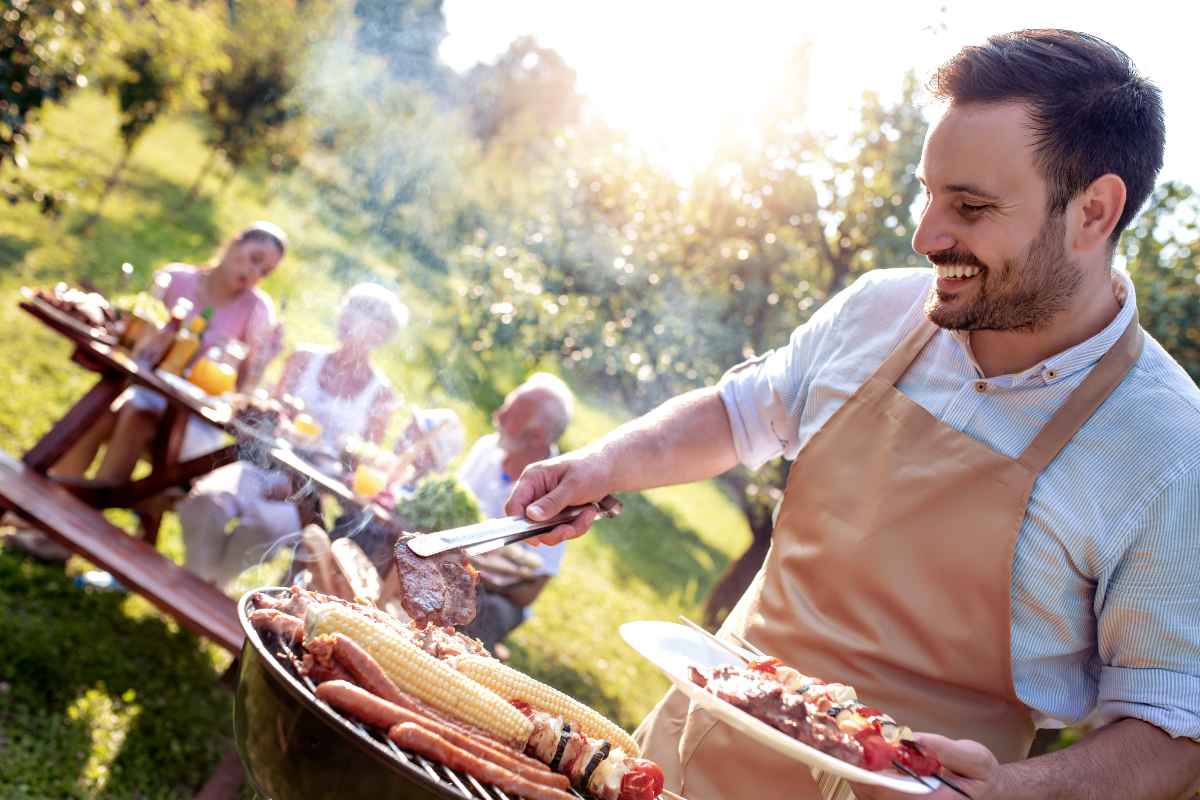 Un uomo che fa il barbecue per la famiglia seduta al tavolo in un giardino