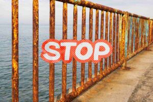 Ringhiere con ruggine ed una scritta stop in primo piano