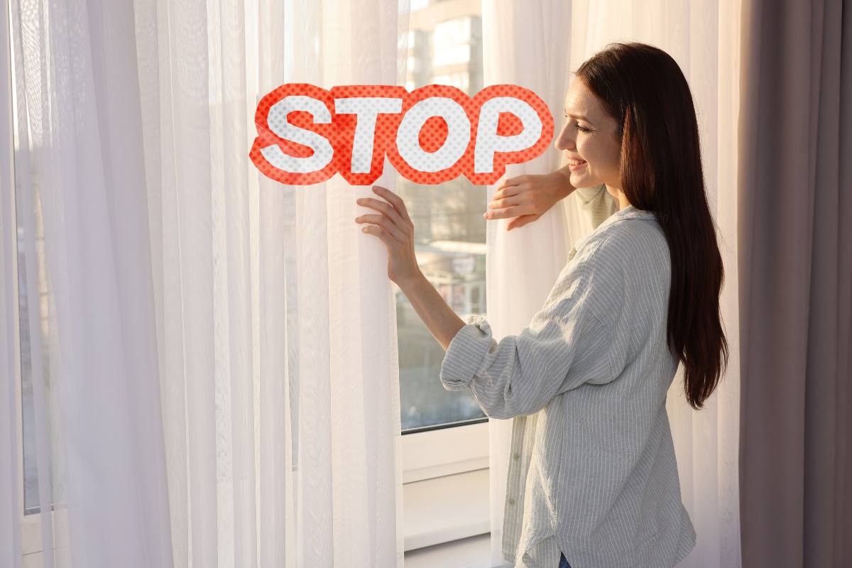 Una ragazza che sposta le tende dalla finestra ed una scritta "Stop"