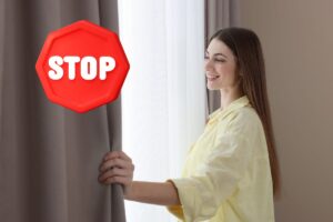 Una donna che sposta le tende ed un simbolo di stop in alto a sinistra