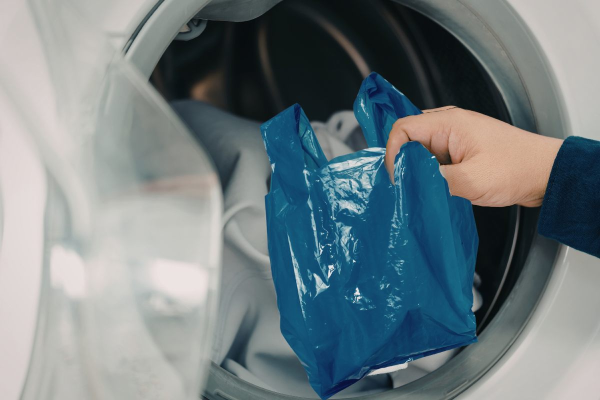 Una persona che mette un sacchetto di plastica in lavatrice