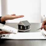 mano con calcolatrice ed altra che firma con case sullo sfondo e fogli