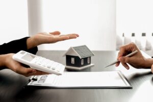 mano con calcolatrice ed altra che firma con case sullo sfondo e fogli