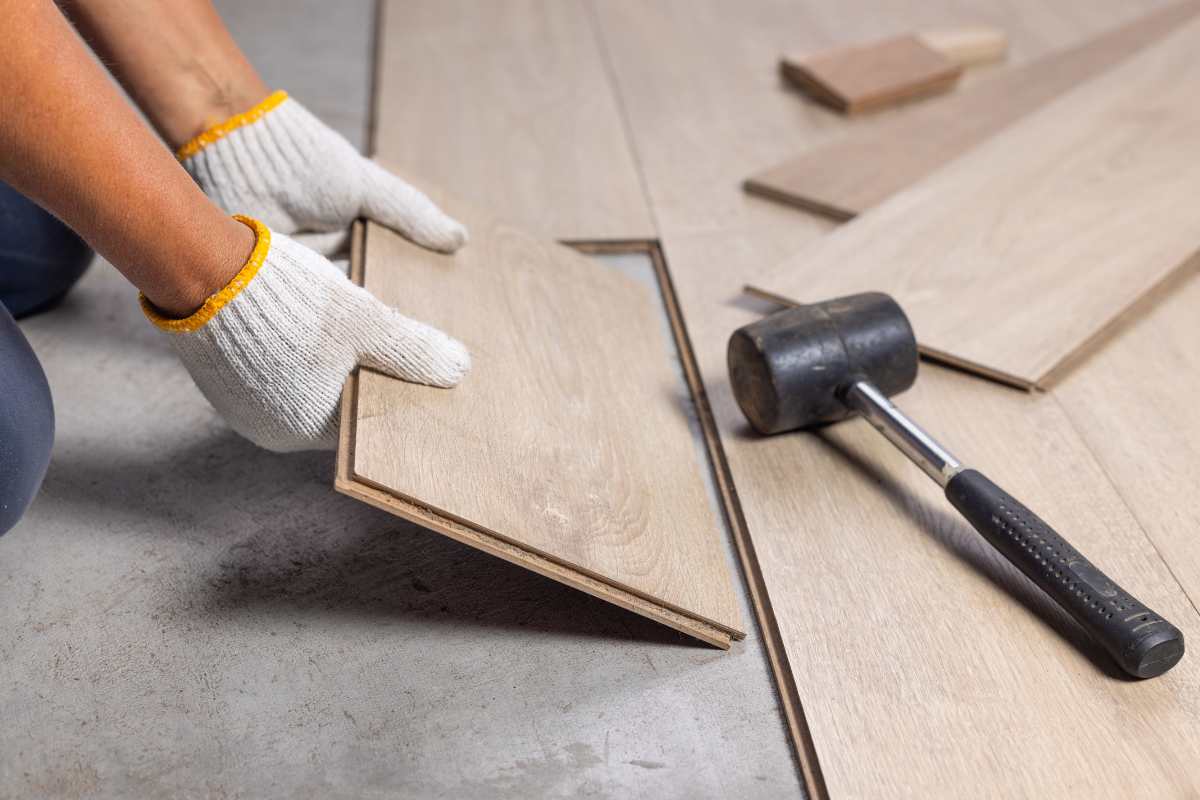 mani che montano pavimento in legno e martello in gomma 