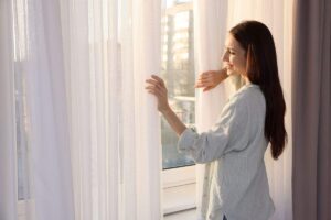 donna sorridente che apre tende bianche in casa