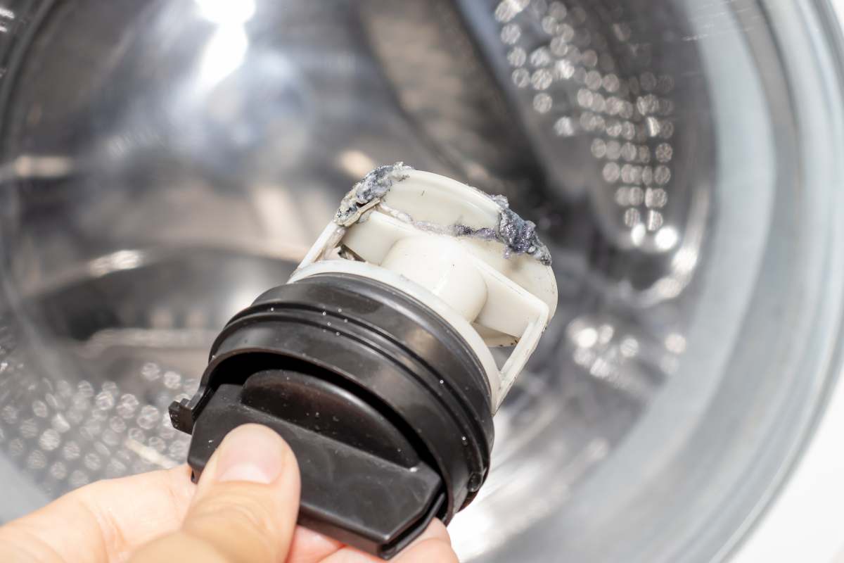 donna con in mano il filtro della lavatrice sporco 