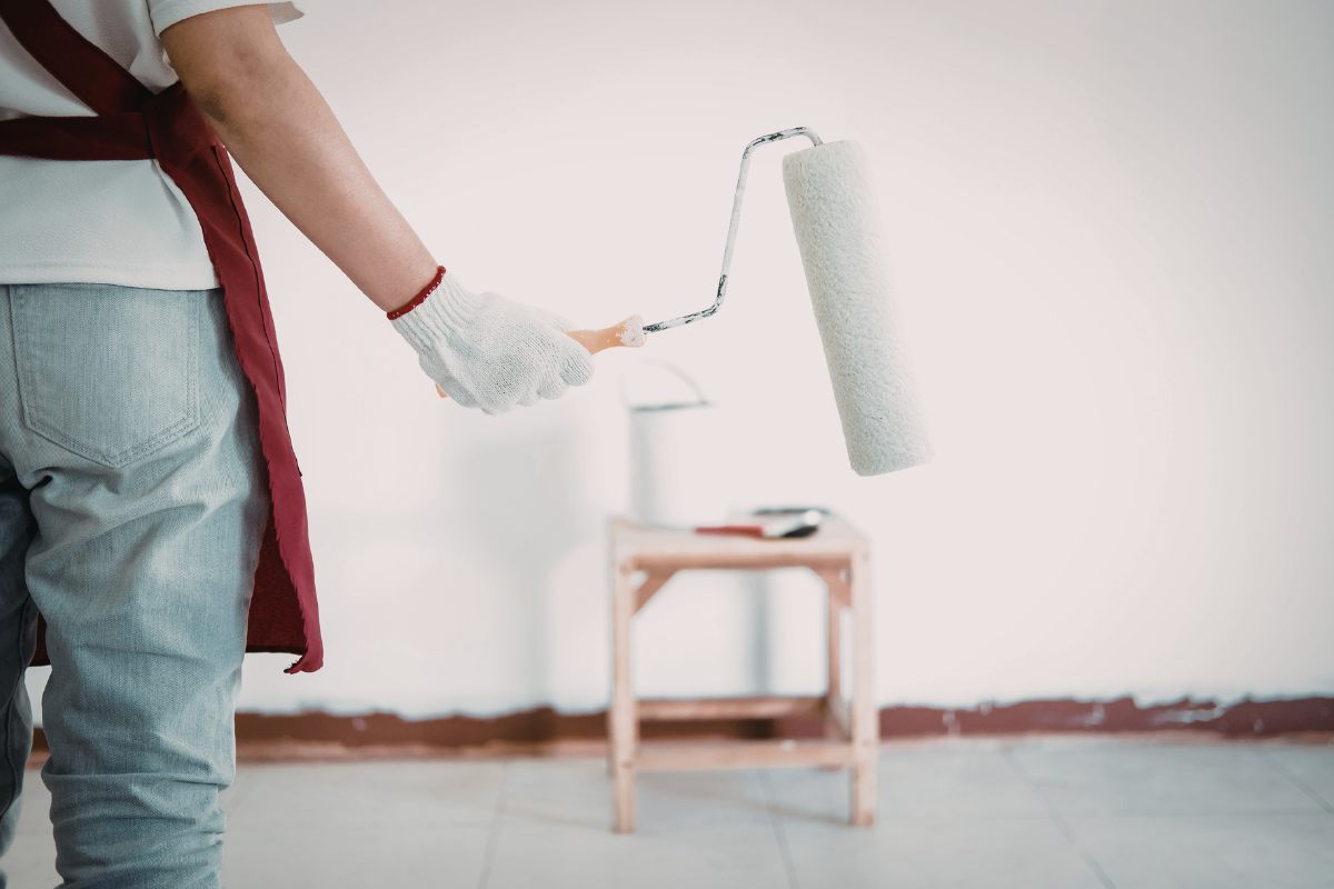 Un imbianchino con un rullo con davanti una parete bianca