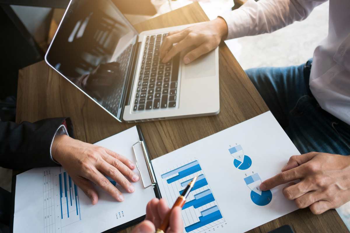 donna e uomo davanti al computer che leggono fogli con grafici 