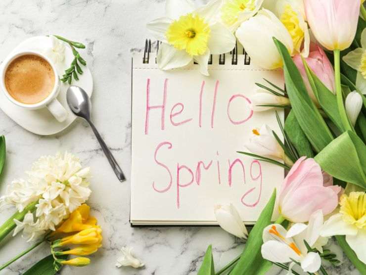 tavolino con tazzina di caffè e block notes su cui c'è scritto 'hello spring'