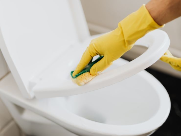 mano con guanto giallo che pulisce tavoletta del wc