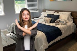 Una camera da letto con poco spazio occupato dal letto ed una ragazza contrariata in primo piano