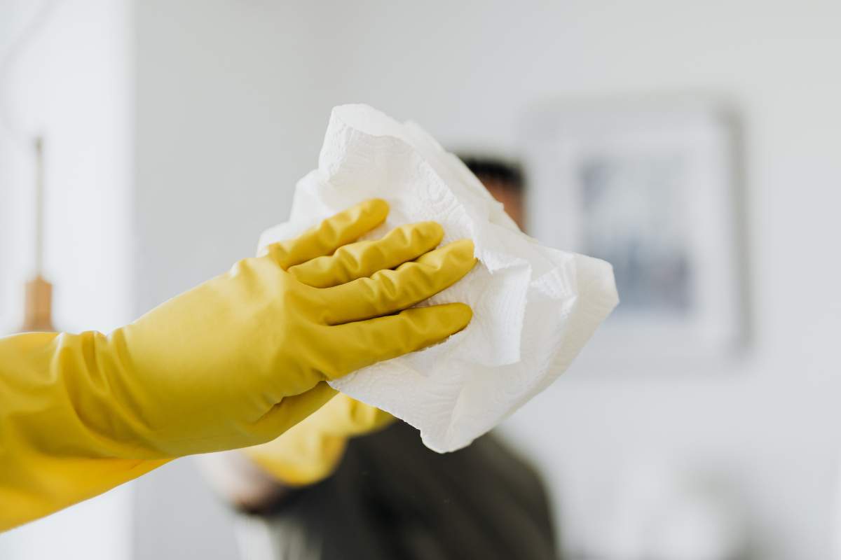 Mano che pulisce vetro con guanto giallo 