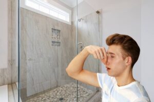 Una doccia ed un uomo che si tappa il naso per la puzza