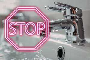 rubinetto con acqua che scorre e scritta stop in rosso