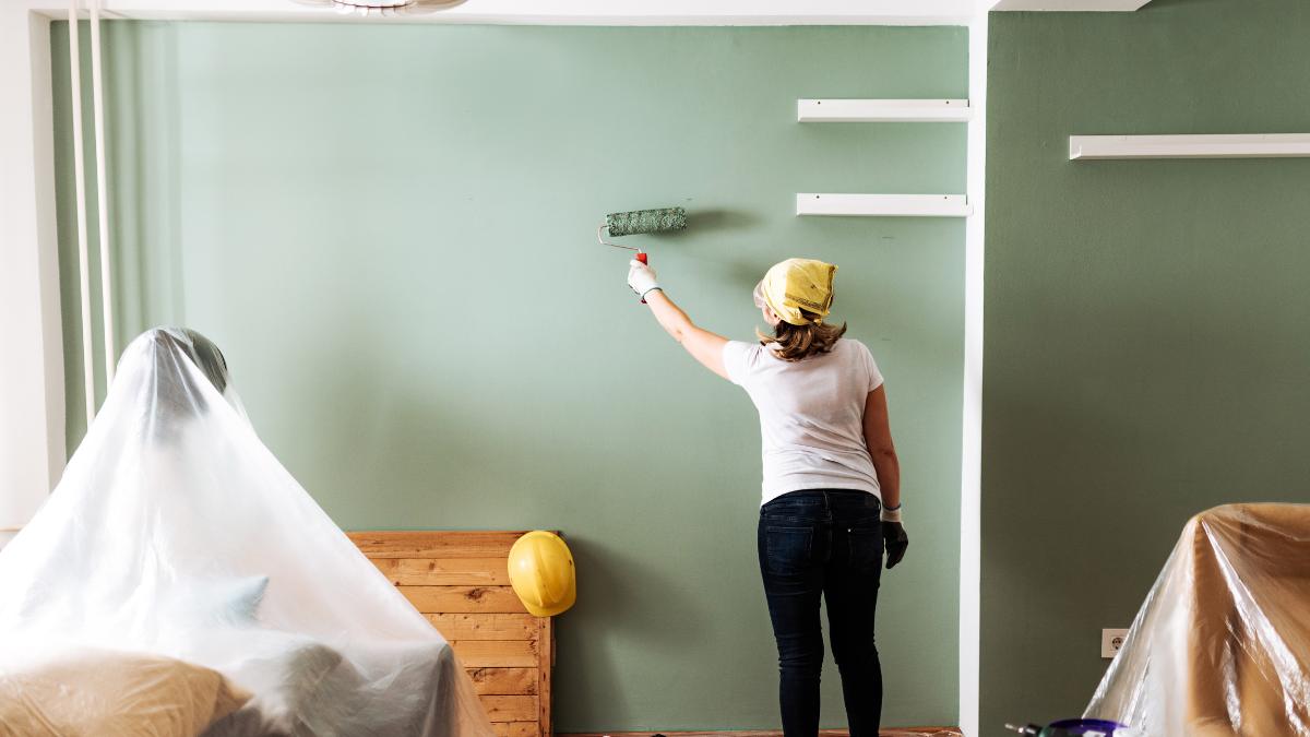 donna che con rullo dipinge camera con mobili coperti 