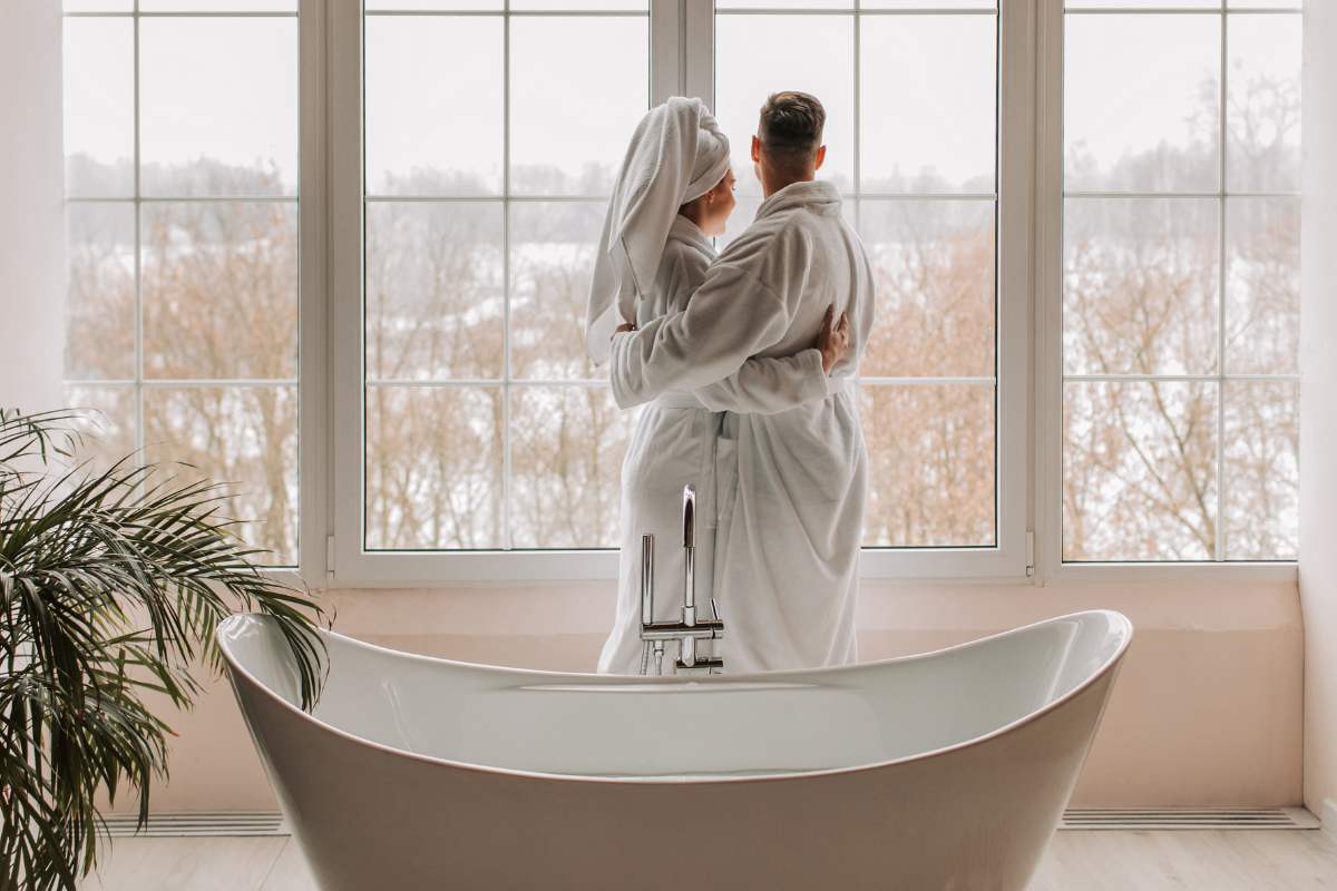 Una coppia entrambi in accappatoio che si abbraccia davanti ad una vasca da bagno