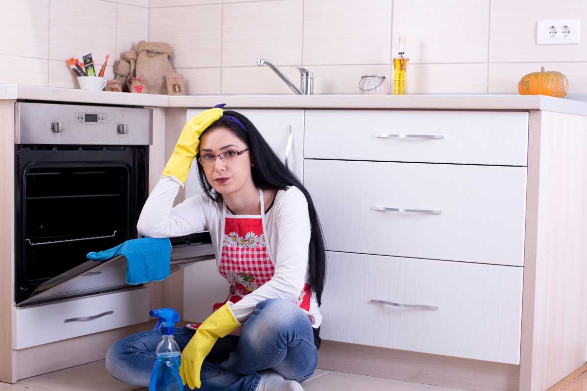 donna disperata seduta vicino al forno aperto con prodotti per la pulizia