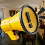 soggiorno con megafono giallo al centro e simbolo attenzione