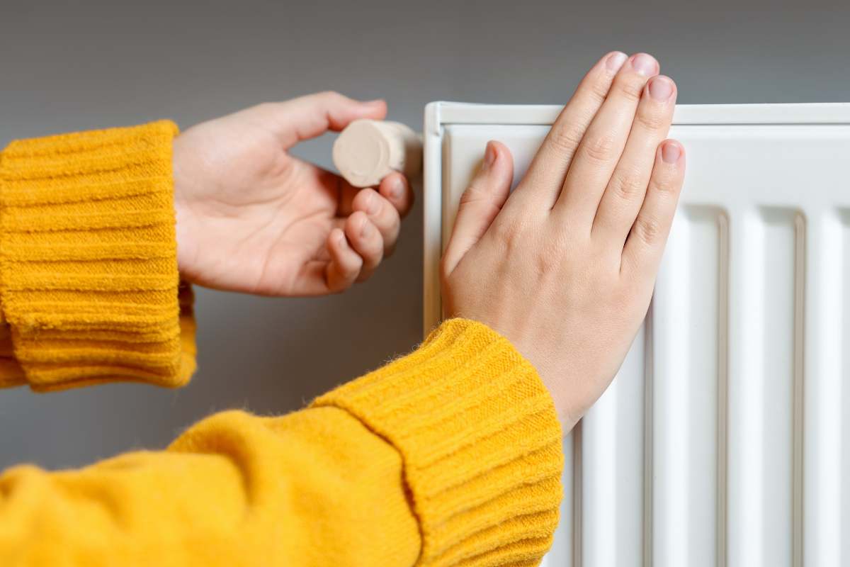 termosifone e donna con mano sopra e maglione giallo 