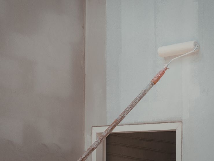 rullo che usa colore bianco per tinteggiare parete di casa