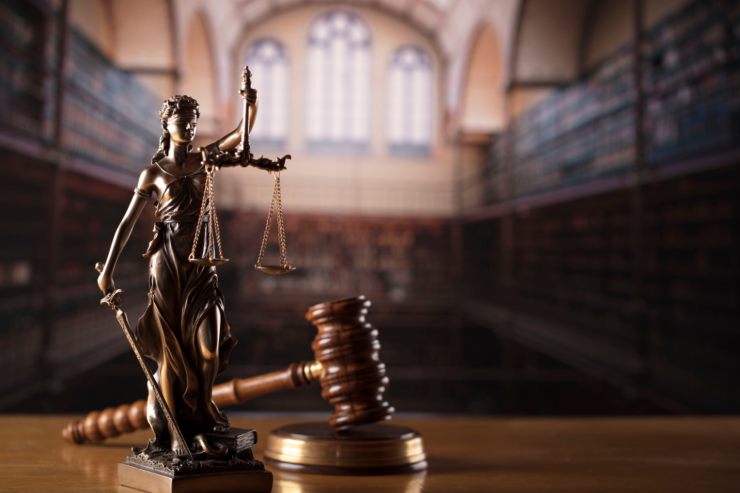 Un tribunale con in primo piano una statua di giustizia e un martello da giudice